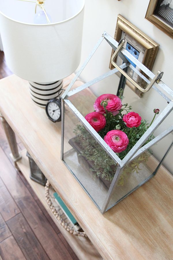 a glass box with flowers in it sitting on a table next to a clock and lamp