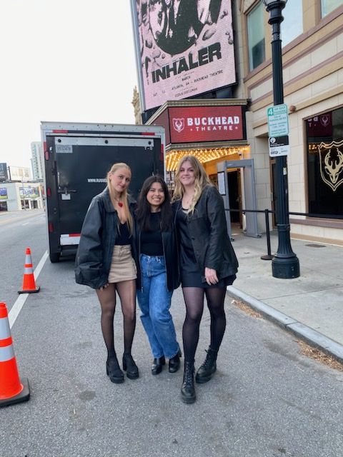 three women standing in front of a movie theater on the side of a road with traffic cones around them