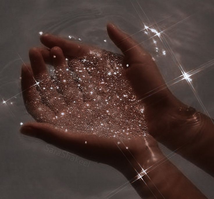 a person's hand is shown in the water with sparkling stars on it and sparkles all over them