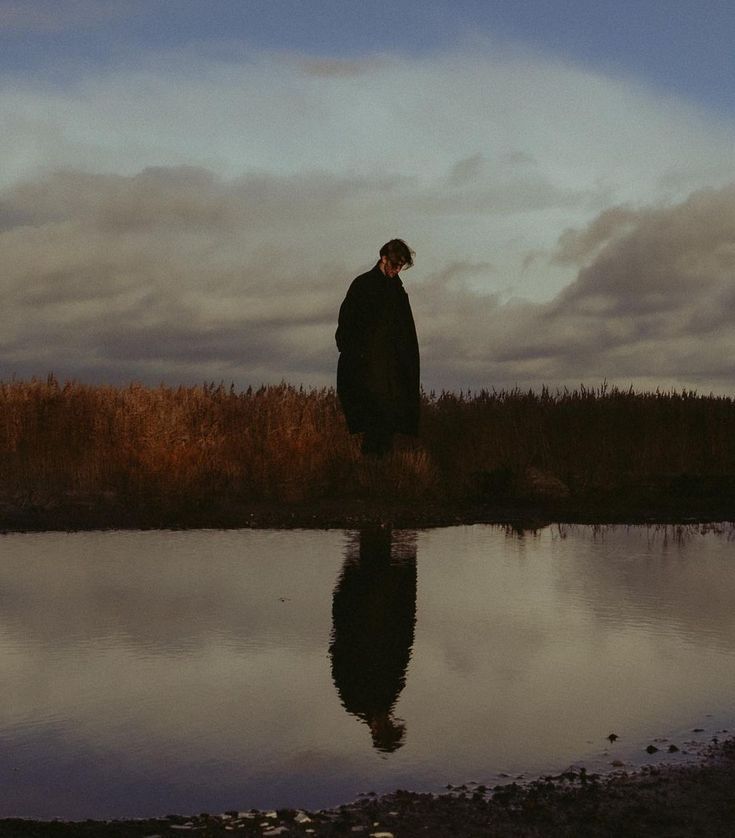 a man standing on the edge of a body of water with his reflection in the water