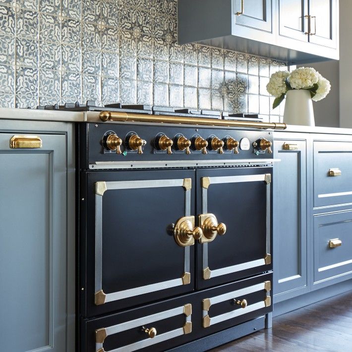 an old fashioned stove in the middle of a kitchen with blue cabinets and gold knobs