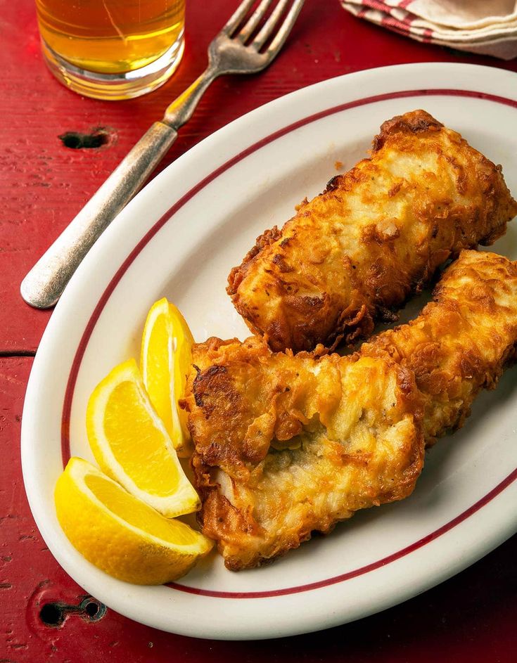 two fried food items on a plate with lemon wedges