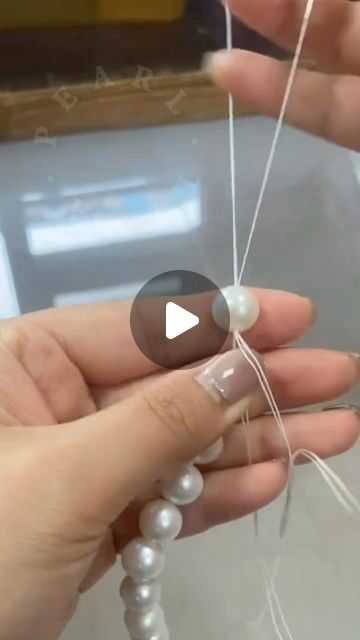 two hands are holding beads and threading them with white string on the end of each bead