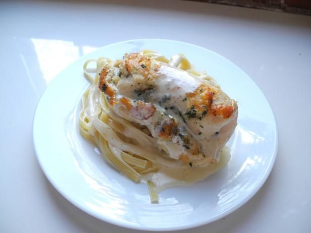 a white plate topped with pasta covered in sauce and chicken breast on top of it