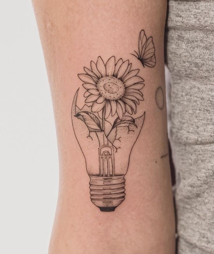 a sunflower in a light bulb tattoo on the right side of the arm with butterflies flying around it