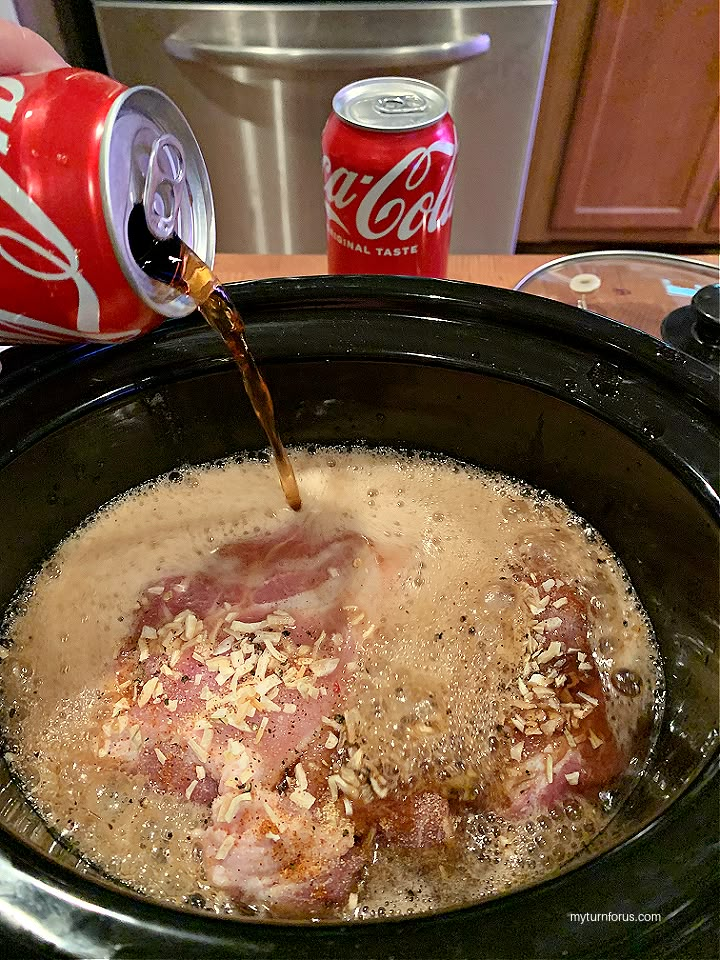 a slow cooker filled with food next to a can of soda