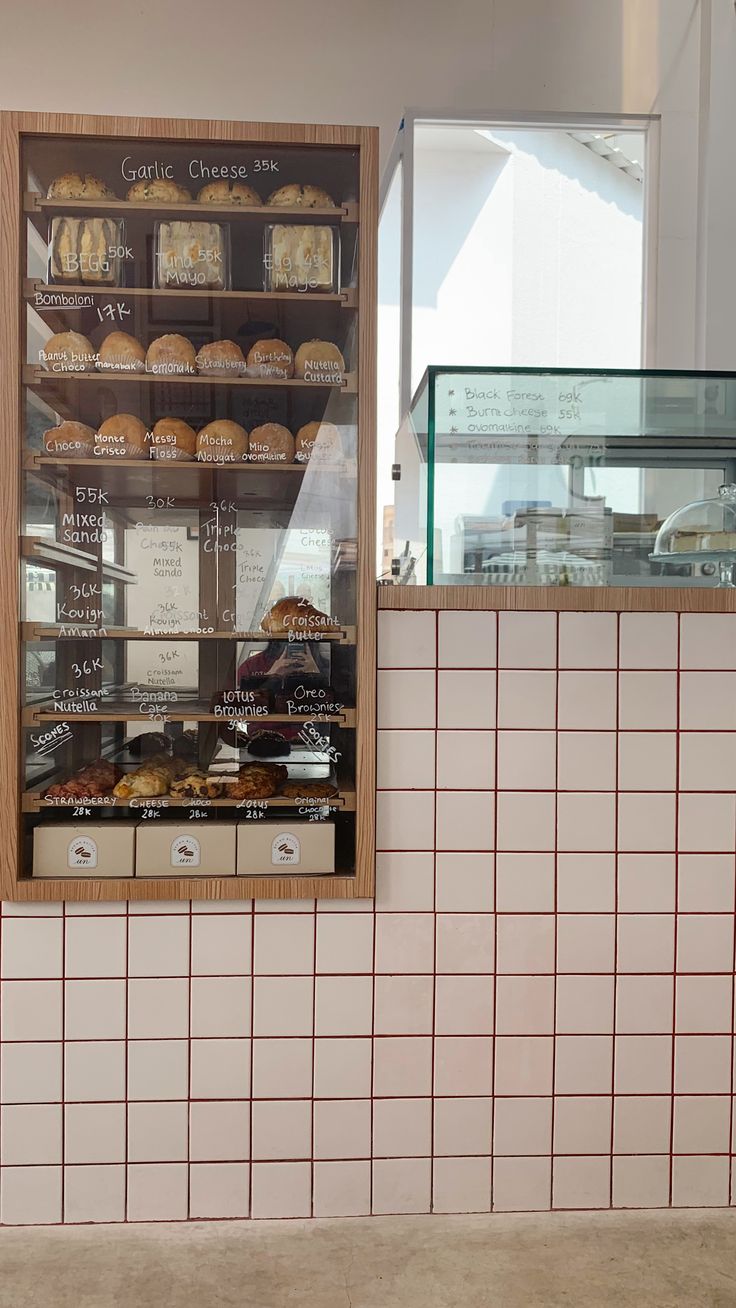 a bakery display case filled with lots of pastries and donuts in front of a white tiled wall