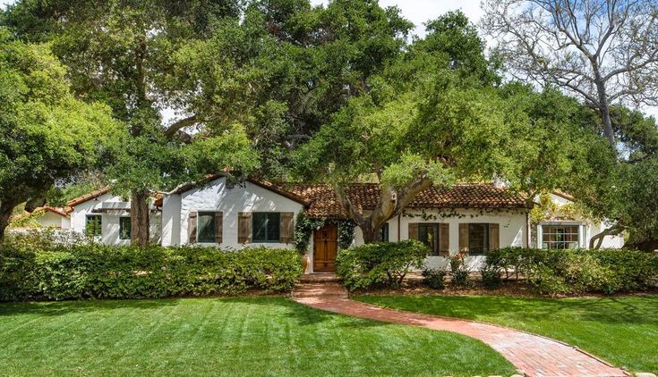 a white house surrounded by lush green trees and grass in front of it is a brick walkway leading to the front door