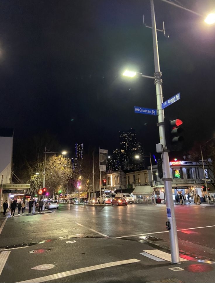 an empty street at night with people walking on the sidewalk and cars driving down the road