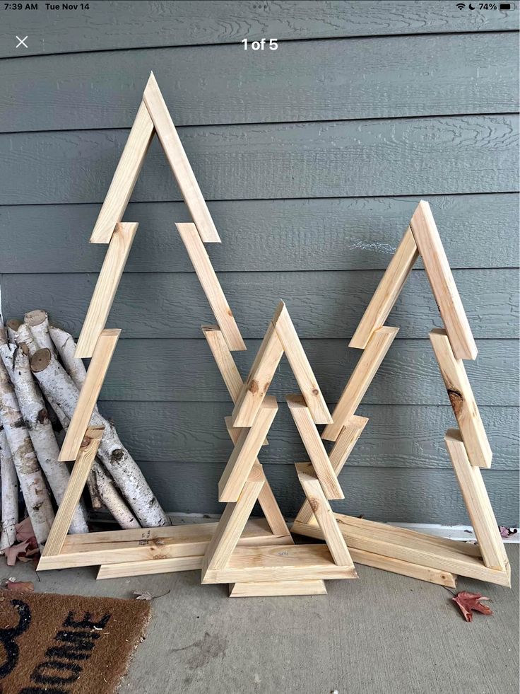 three wooden christmas trees sitting next to each other on top of a rug in front of a house