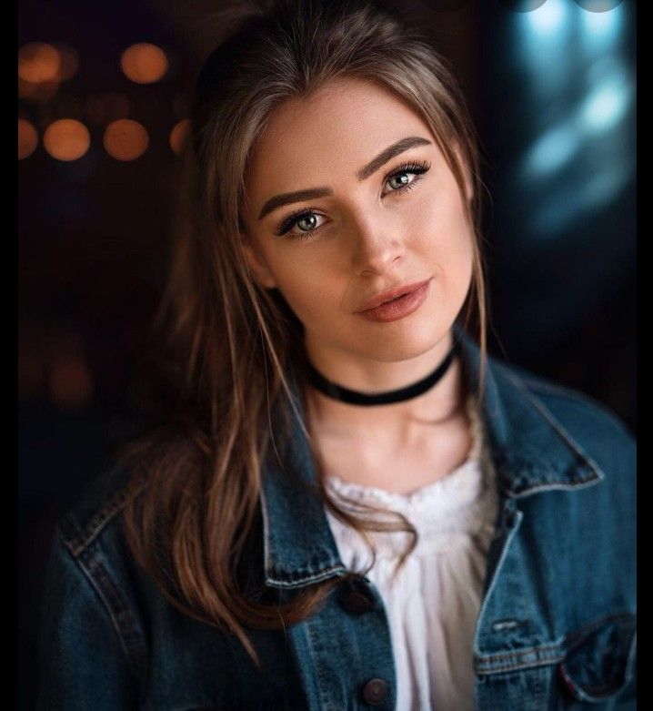 a woman with long hair wearing a denim jacket and white shirt is looking at the camera