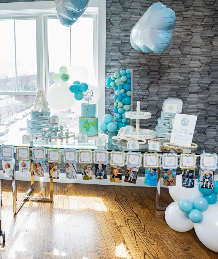 a table with balloons and pictures on it in front of a window at a baby's first birthday party