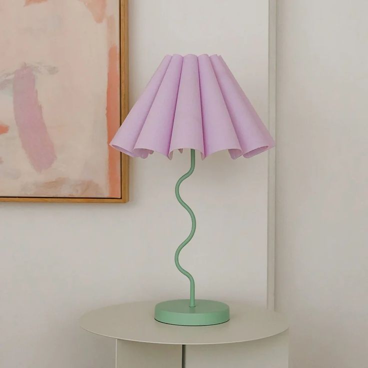 a pink lamp sitting on top of a white table next to a painting hanging above it