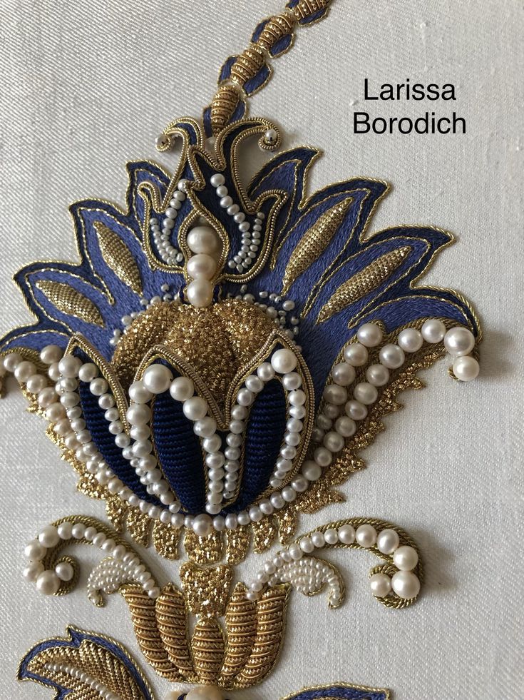 a blue and gold brooch with pearls on it's side, sitting on a white cloth