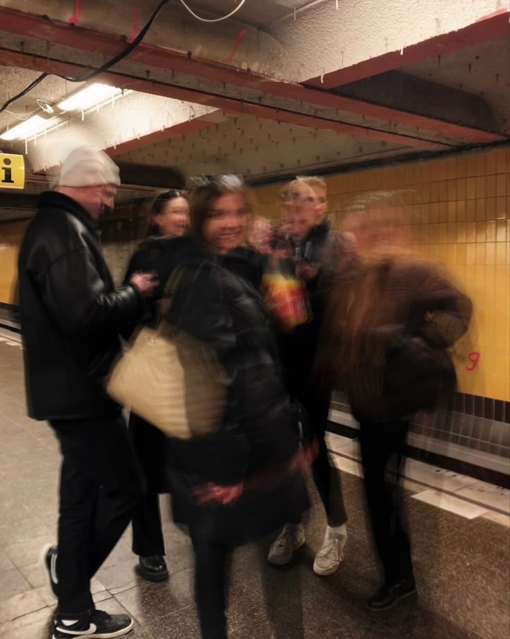 a group of people standing next to each other near a train station platform with a sign on the wall