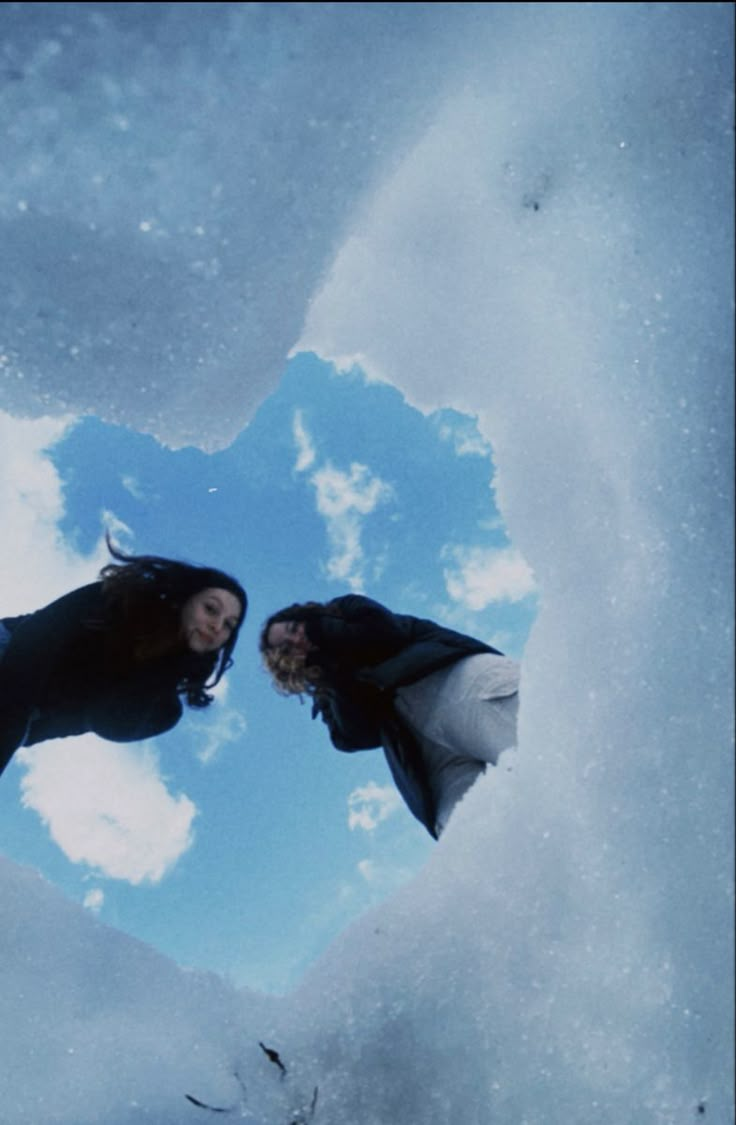 two women are standing in the middle of a heart - shaped hole with snow on it