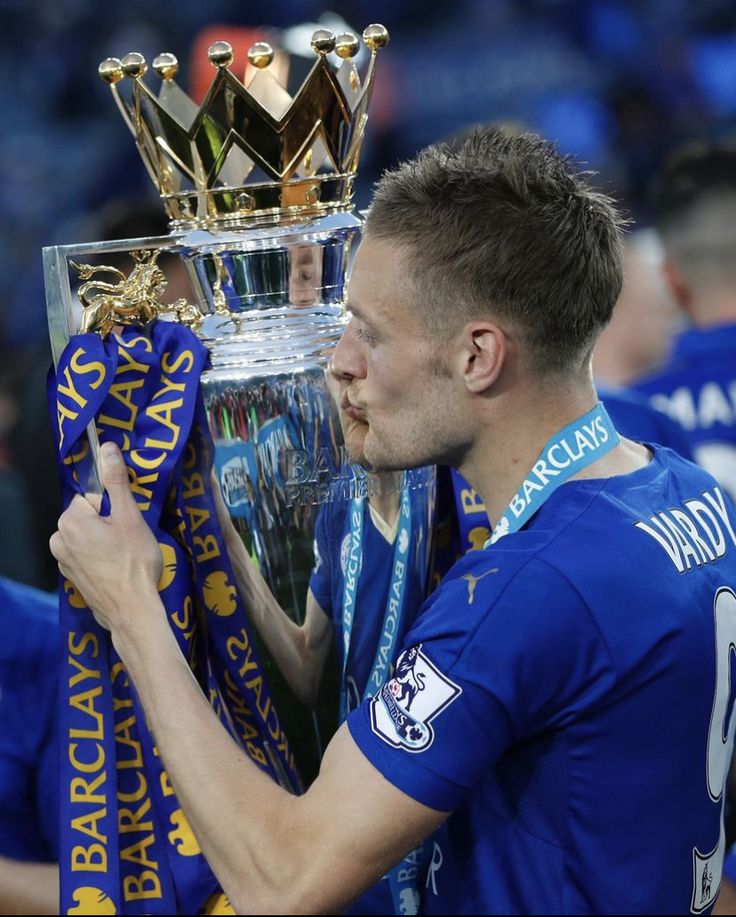 a man holding up a trophy in front of his face while wearing a blue shirt