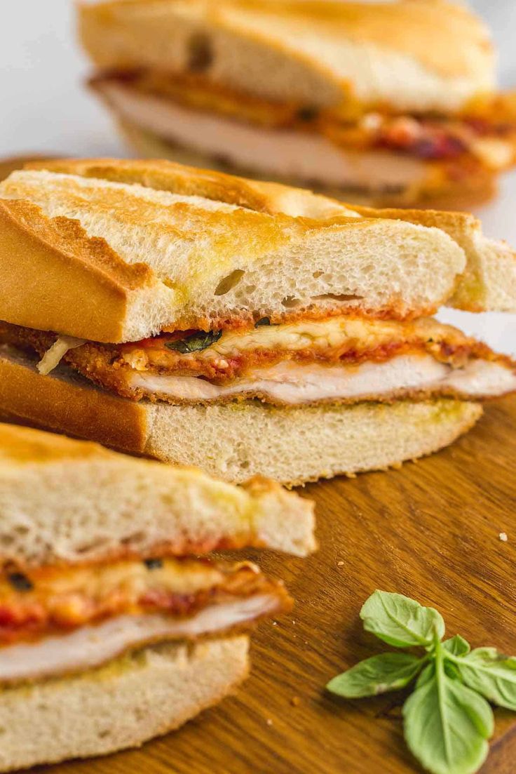 a cut in half sandwich sitting on top of a wooden cutting board next to fresh basil