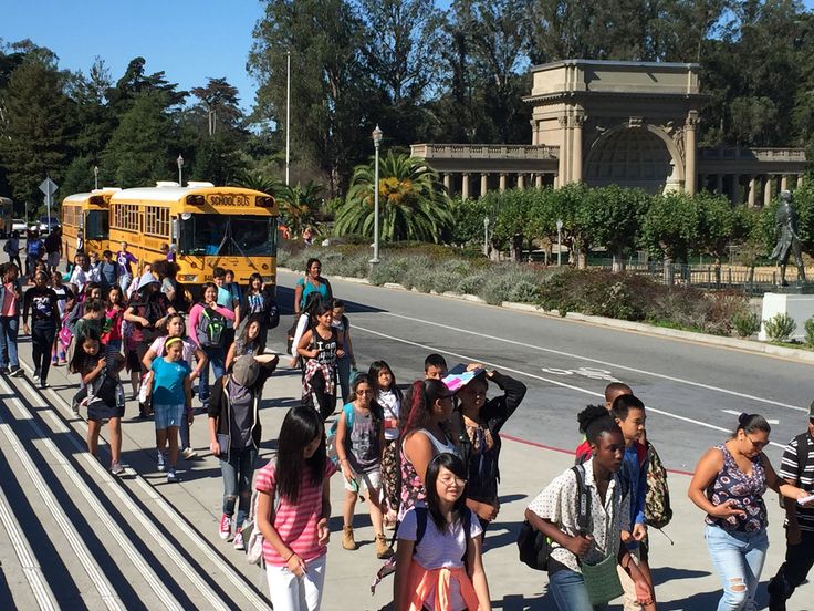 many people are walking on the sidewalk near a school bus