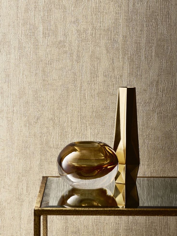 a glass vase sitting on top of a table next to a gold colored wallpaper