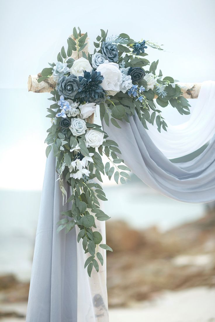 a wedding arch decorated with flowers and greenery on the beach in front of the ocean