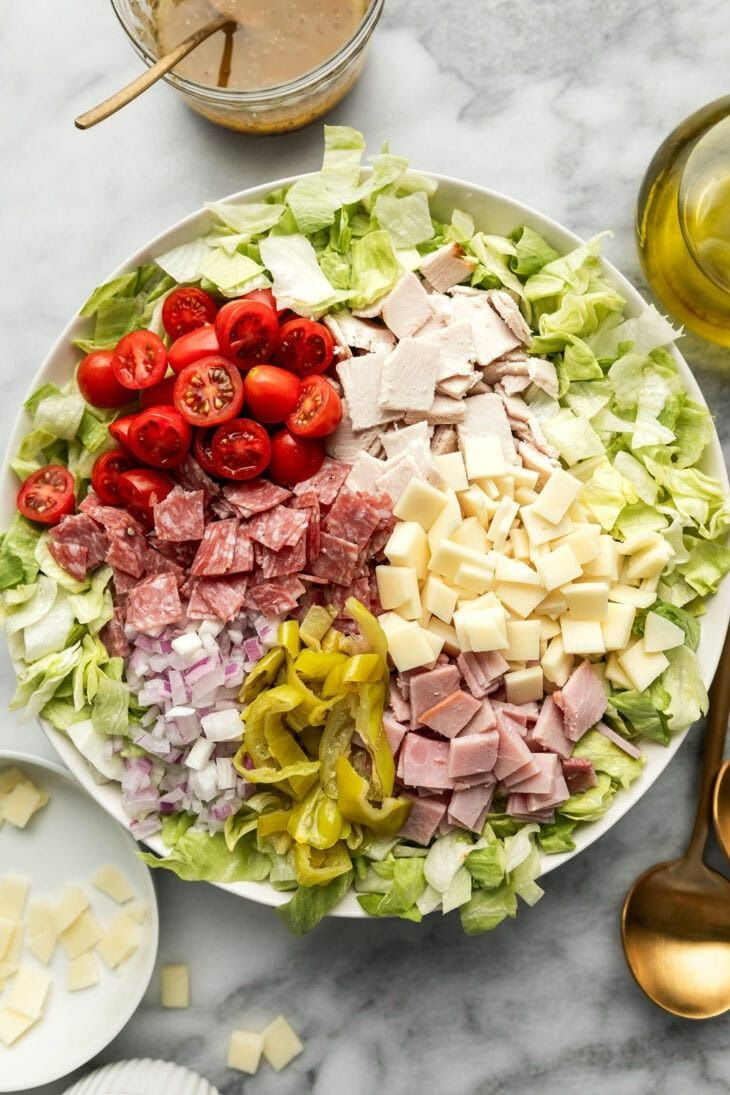 a salad with ham, lettuce, tomatoes and cheese on it next to other ingredients