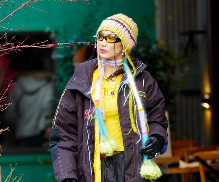 a woman wearing sunglasses and a yellow sweater is standing in front of a tree with her hands on her hips