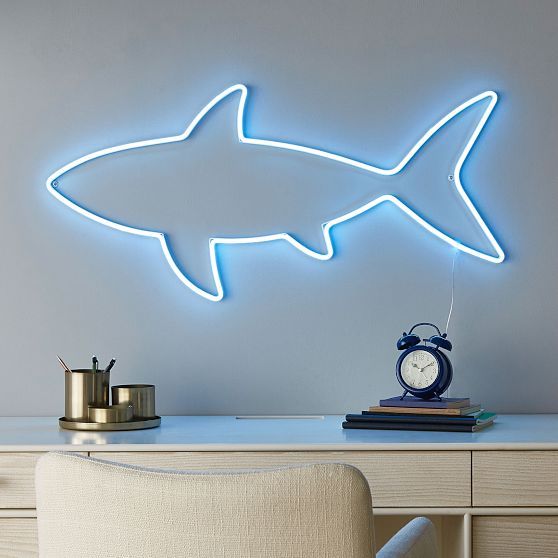 a shark shaped neon sign on the wall above a desk with a clock and lamp