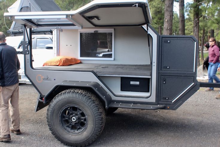 an off road camper is parked in the parking lot with people standing around it