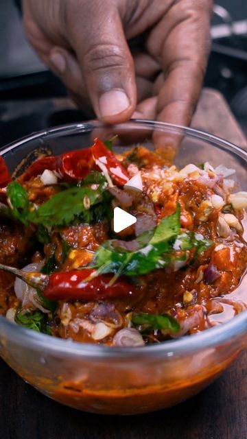 a bowl filled with lots of food on top of a wooden table next to a person's hand