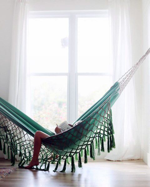 a woman sitting in a hammock reading a book on the window sill