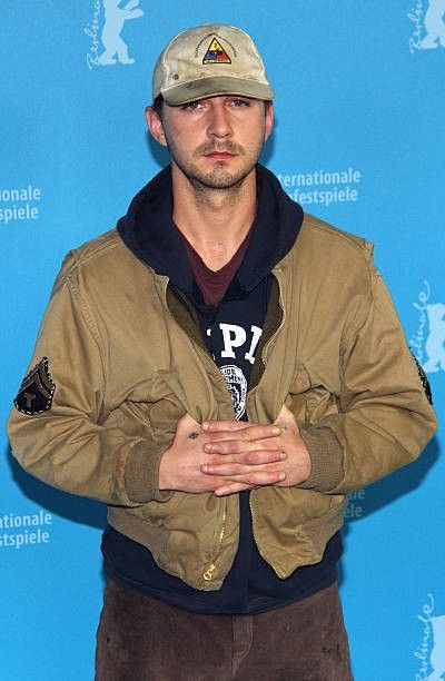 a man standing in front of a blue wall with his hands crossed and looking at the camera