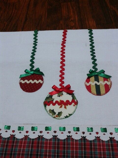 three christmas ornaments hanging from a table cloth on top of a wooden floor with red and green trimmings