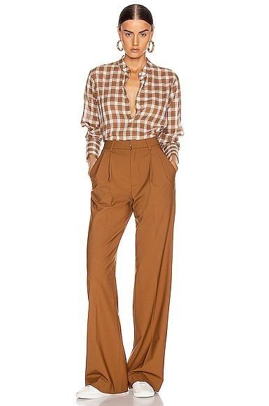 a woman standing in front of a white background wearing brown pants and a checkered shirt