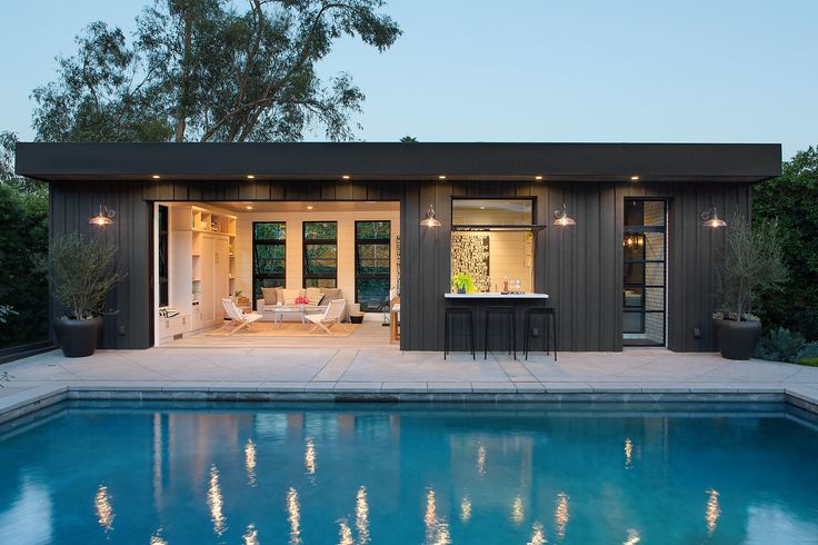 a pool house with an outdoor kitchen and dining area next to the pool at dusk