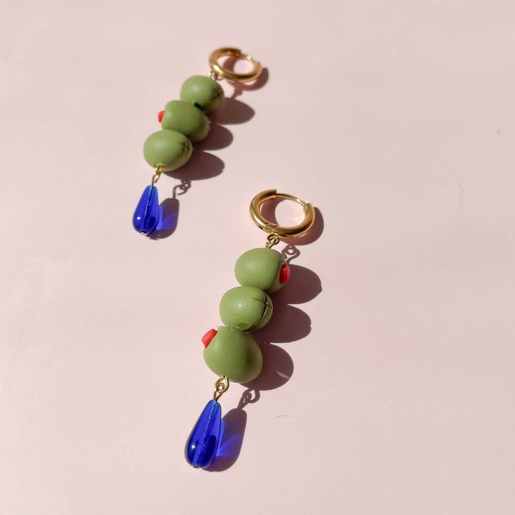 Handmade polymer clay olive earrings! Six mini olives and cobalt glass beads. Hardware is stainless steel, safe for sensitive ears and tarnish resistant. Measures 2.5 in x .5 in Eclectic Green Jewelry With Colorful Beads, Olive Green Earrings, Playful Green Drop Earrings, Playful Multicolor Earrings, Olive Earrings, Bar Apron, Stack Earrings, Hair Necklace, Candle Wrap