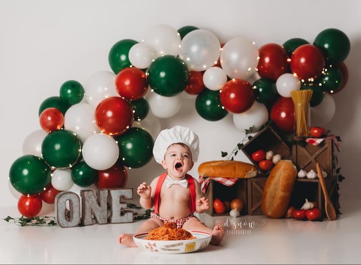 a baby sitting in front of a cake and balloons