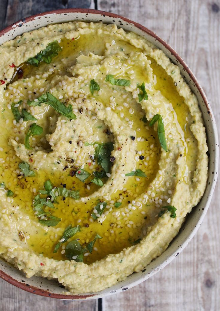 a bowl filled with hummus and herbs on top of a wooden table