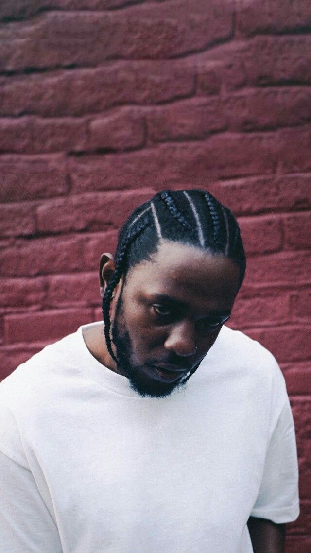 a man with dreadlocks standing in front of a brick wall