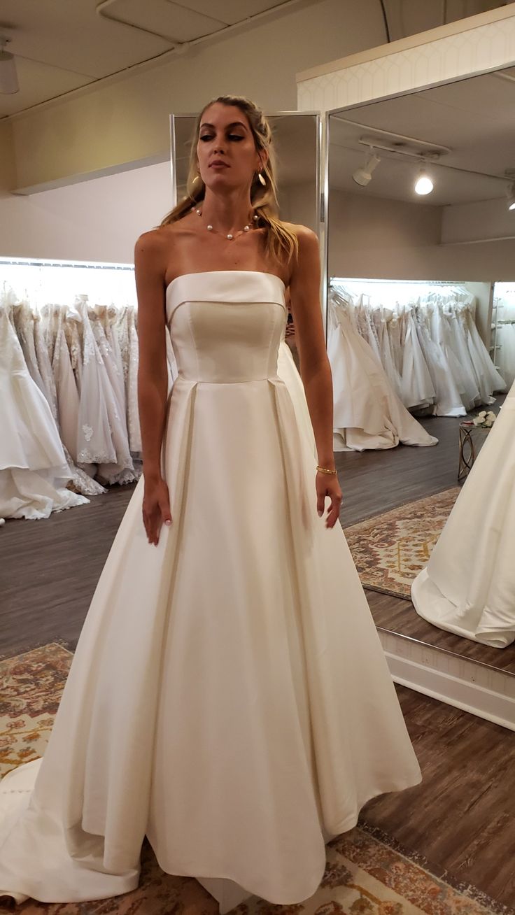 a woman standing in front of a mirror wearing a white wedding dress and looking at the camera