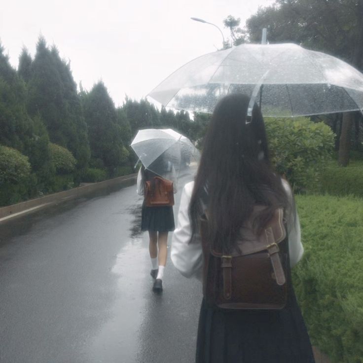 two people walking down the road with umbrellas in hand and one person carrying a backpack