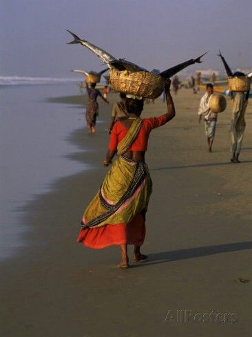 people walking along the beach carrying baskets on their heads