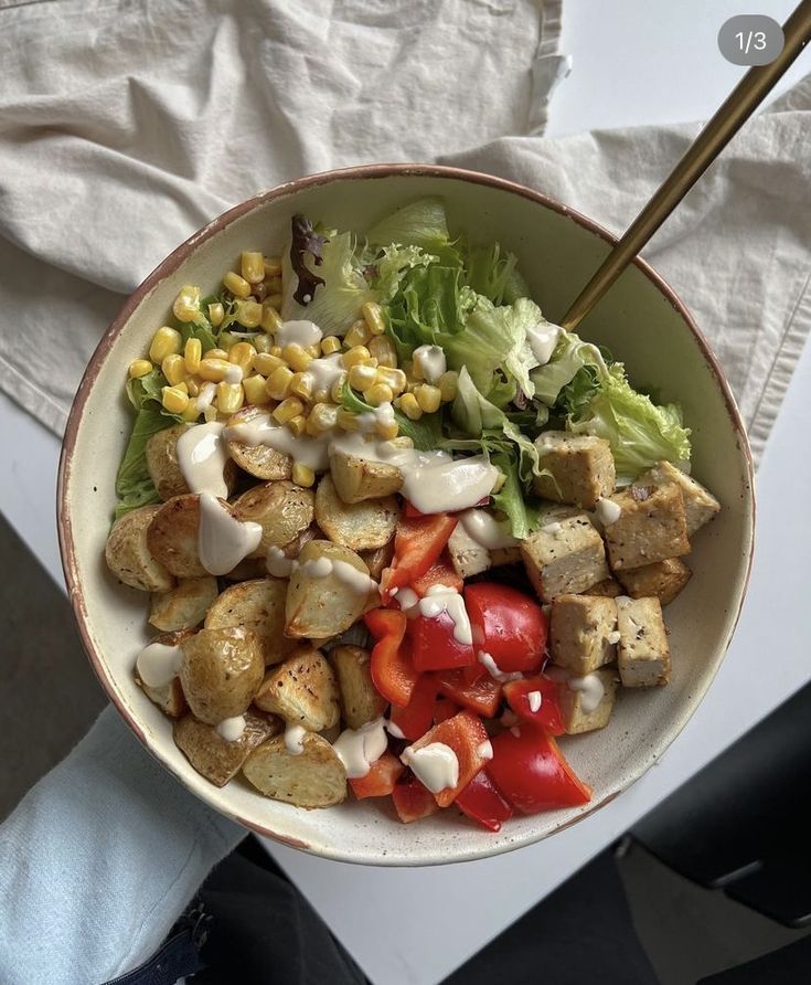 a bowl filled with vegetables and tofu on top of a white table cloth next to a knife