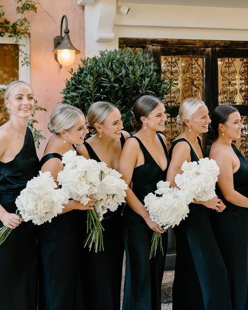 a group of women standing next to each other holding bouquets in front of a building