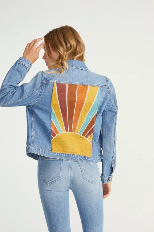 a woman wearing a jean jacket with the sun painted on it