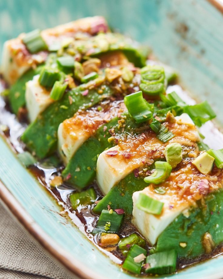 some food is sitting on a plate with sauce and green onions in it, ready to be eaten