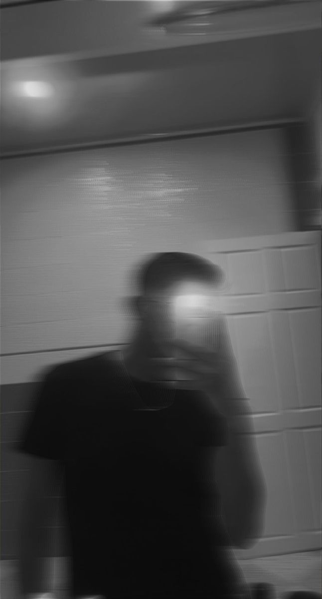 a blurry image of a man in a black shirt and hat standing next to a wall