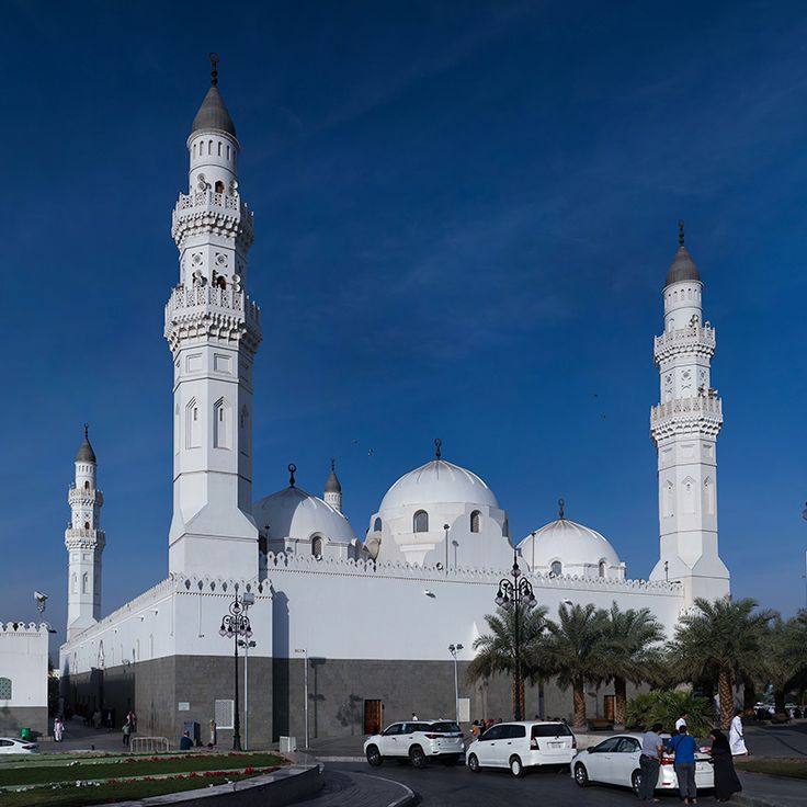 two white cars are parked in front of a large building with three minarets