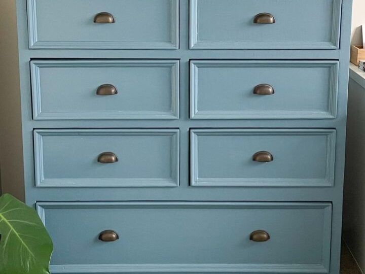 a blue dresser with many drawers on it and a plant in the corner next to it