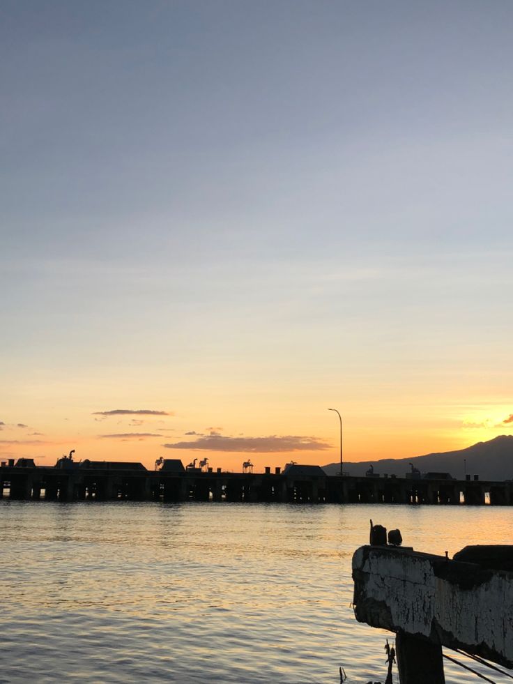 the sun is setting over some water with buildings and hills in the backround